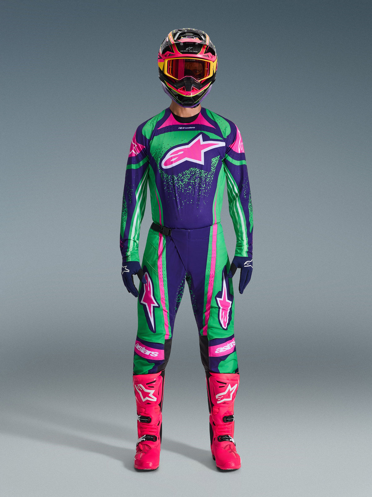 Alpinestars 2026 Techstar Nomur Gear Set, Motocross Racing Outfit, Vibrant Green Purple and Pink, Large Star Logo on Chest and Thighs, Black Helmet with Pink and Yellow Accents, Bright Pink Boots, Professional Sporty Design