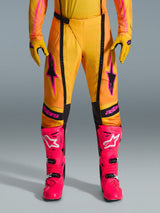 Alpinestars 2026 Techstar Nomur broek, motorcross broek, oranje, geel en roze, gedragen met bijpassende gele handschoenen en felroze racelaarzen, voorzien van zwarte panelen en opvallende roze Alpinestars-branding, technische off-road race-uitrusting