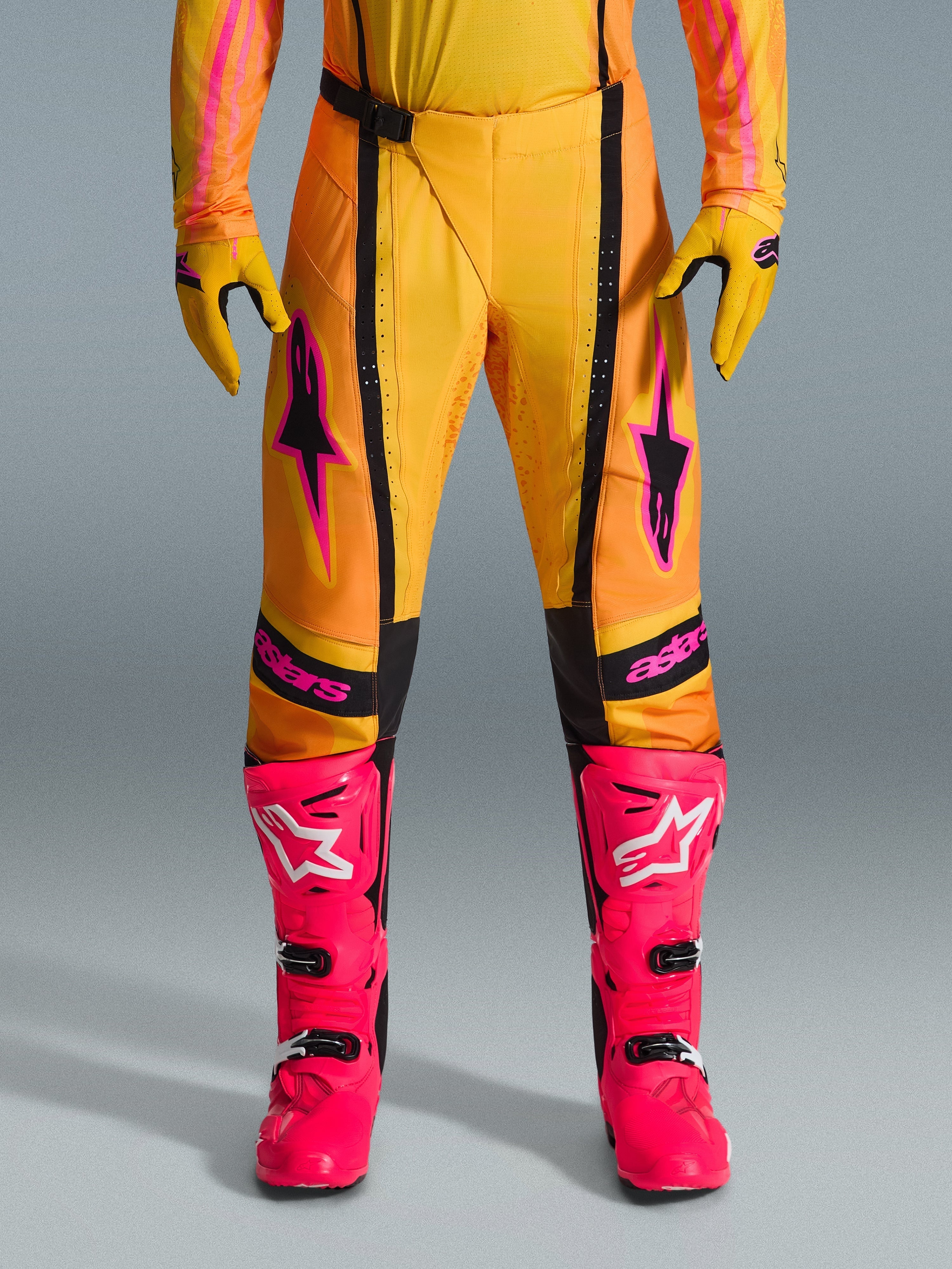 Alpinestars 2026 Techstar Nomur broek, motorcross broek, oranje, geel en roze, gedragen met bijpassende gele handschoenen en felroze racelaarzen, voorzien van zwarte panelen en opvallende roze Alpinestars-branding, technische off-road race-uitrusting