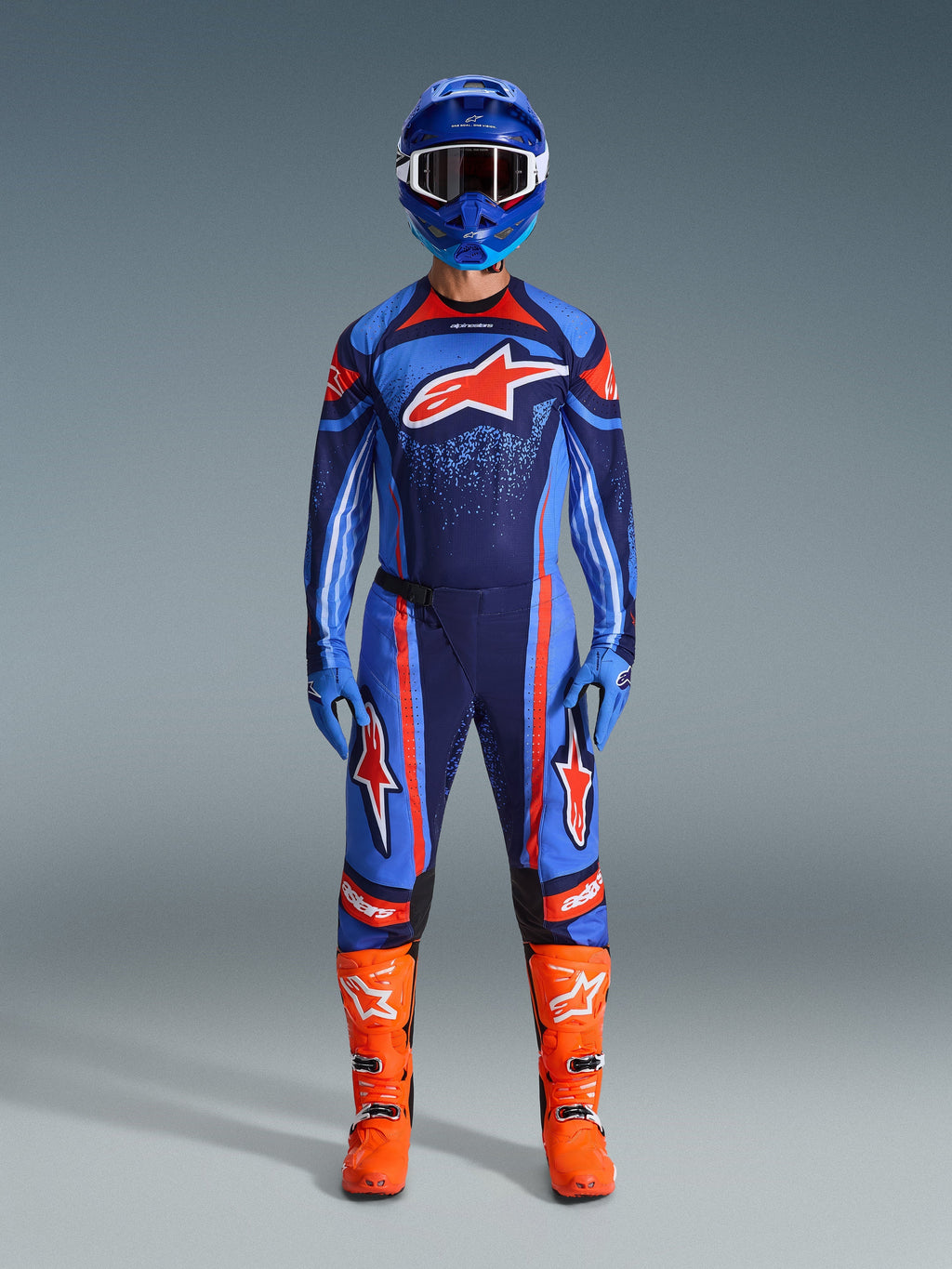 Alpinestars 2026 Techstar Nomur gear set, Motocross rider in full racing kit, Dark Navy with Orange and UCLA Blue accents, matching jersey and pants with large logos, blue helmet and bright orange boots, coordinated off-road competition gear.