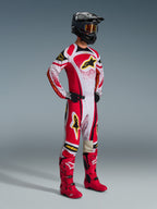 Motocross rider wearing complete racing gear, 2026 Techstar Nomur Jersey in Red, White, and Black, matching motocross pants with yellow accents, black helmet with goggles, red boots, and black gloves, coordinated outfit for off-road racing