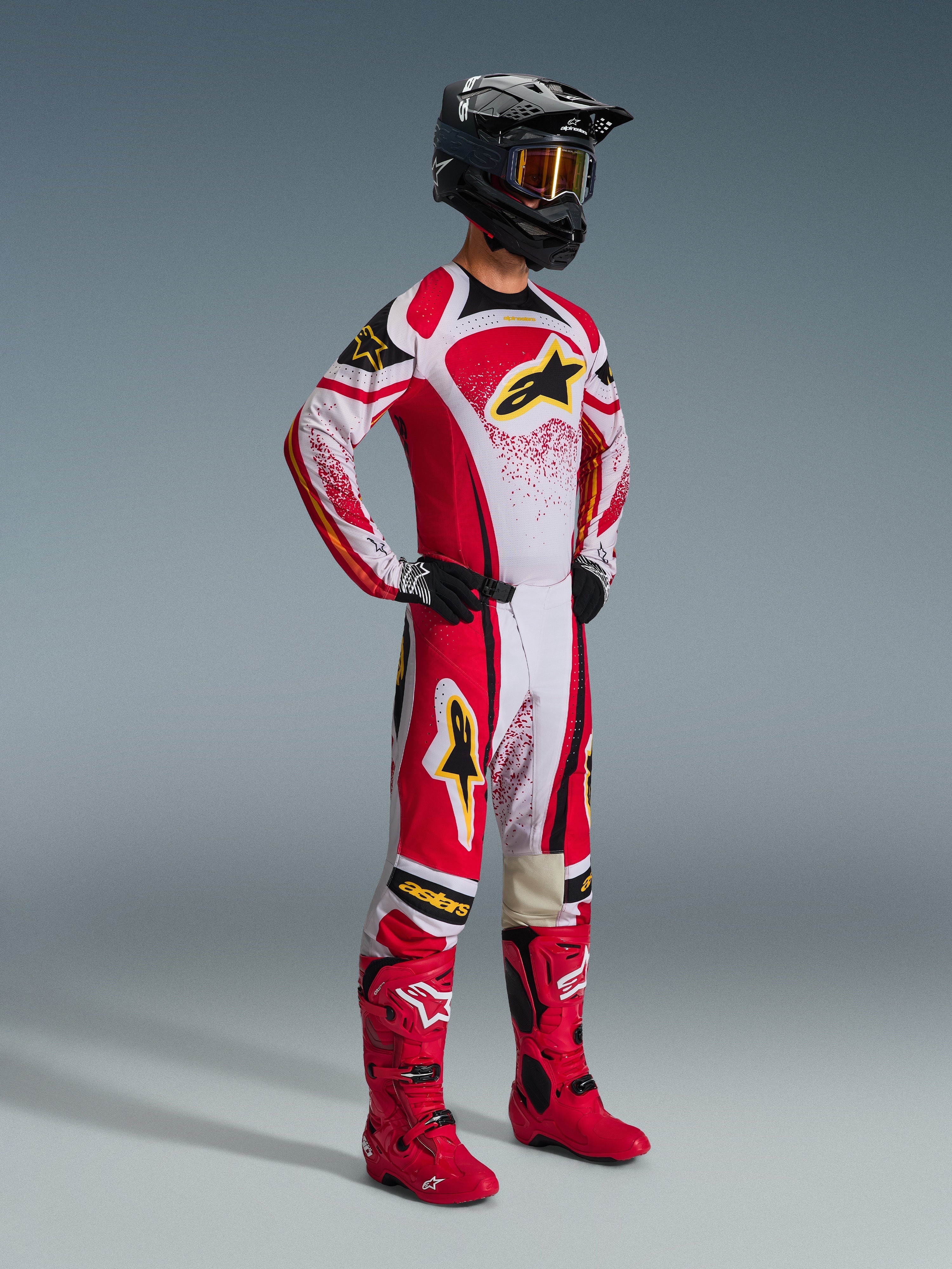Motocross rider wearing complete racing gear, 2026 Techstar Nomur Jersey in Red, White, and Black, matching motocross pants with yellow accents, black helmet with goggles, red boots, and black gloves, coordinated outfit for off-road racing