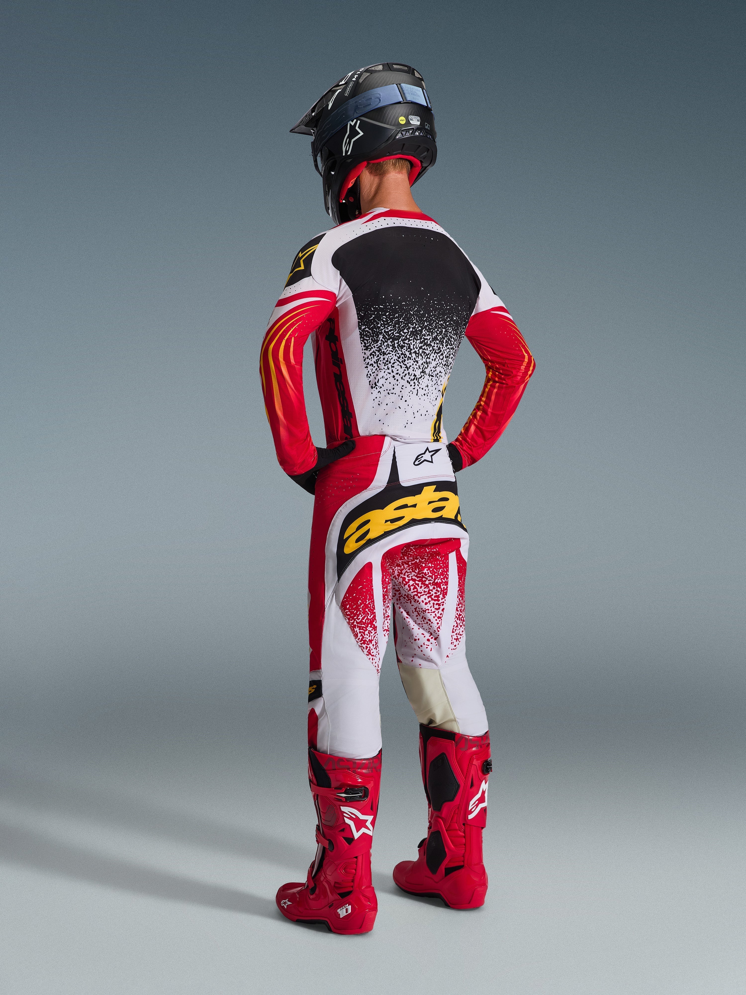 Motocross rider seen from the back wearing the 2026 Techstar Nomur Jersey in Red and Light Gray, matching racing pants with bold yellow branding, red off-road boots, and a black helmet, complete professional motocross gear set.