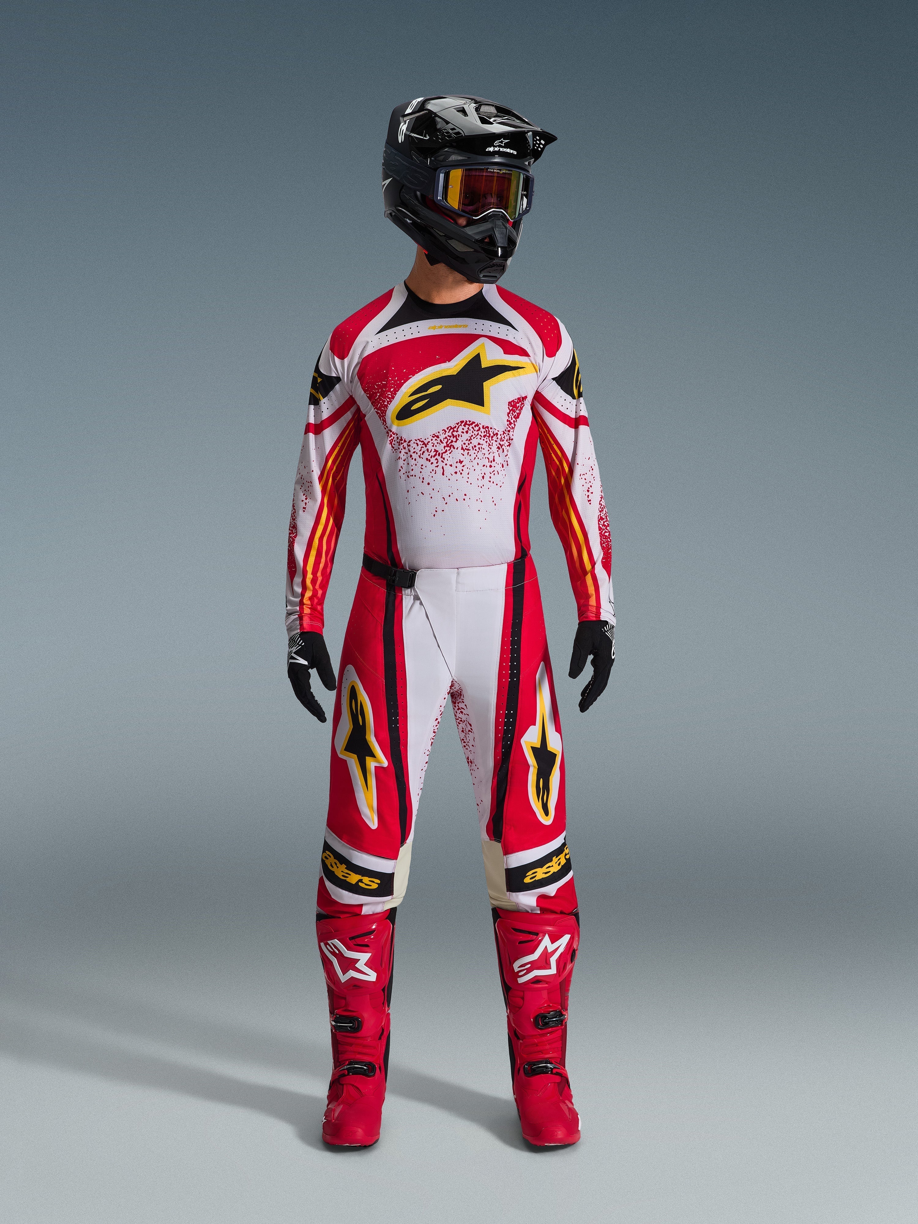 Alpinestars 2026 Techstar Nomur Jersey, Red and White with Black accents and Yellow logos, worn by a motocross rider with matching pants, red boots, and a black helmet, professional off-road racing gear