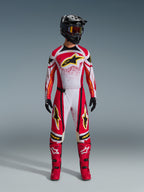 Motocross rider wearing Alpinestars 2026 Techstar Nomur Pants, Red White and Black off-road racing gear, matching jersey with yellow star logo, black helmet with goggles, red boots, and black gloves, coordinated outfit for motocross