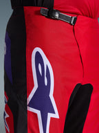 Alpinestars 2026 Fluid Grid broek, motorcross broek, rood, zwart en paars, close-up van de taille en heupen met een zwart ratelsluitingssysteem en een groot paars Alpinestars sterlogo met witte omlijning, duurzame getextureerde stof voor off-road racen.