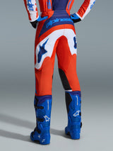 Alpinestars 2026 Fluid Grid Pants, Motocross Pants, Orange and UCLA Blue with white panels, rear view showing bold blue branding on the seat and star logo, paired with matching blue motocross boots, professional off-road racing gear