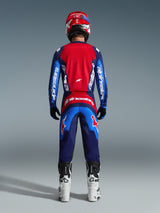 Motocross rider from the back wearing complete racing gear, 2026 Fluid Grid Pants in Blue Red, matching red and blue jersey with Alpinestars branding, red and blue helmet, white and black boots, coordinated outfit for off-road racing
