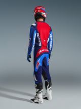 Motocross rider viewed from behind wearing Alpinestars 2026 Fluid Grid Pants in Blue Red, matching blue and red jersey with white logos, red and white helmet, white and black boots, coordinated outfit for off-road racing