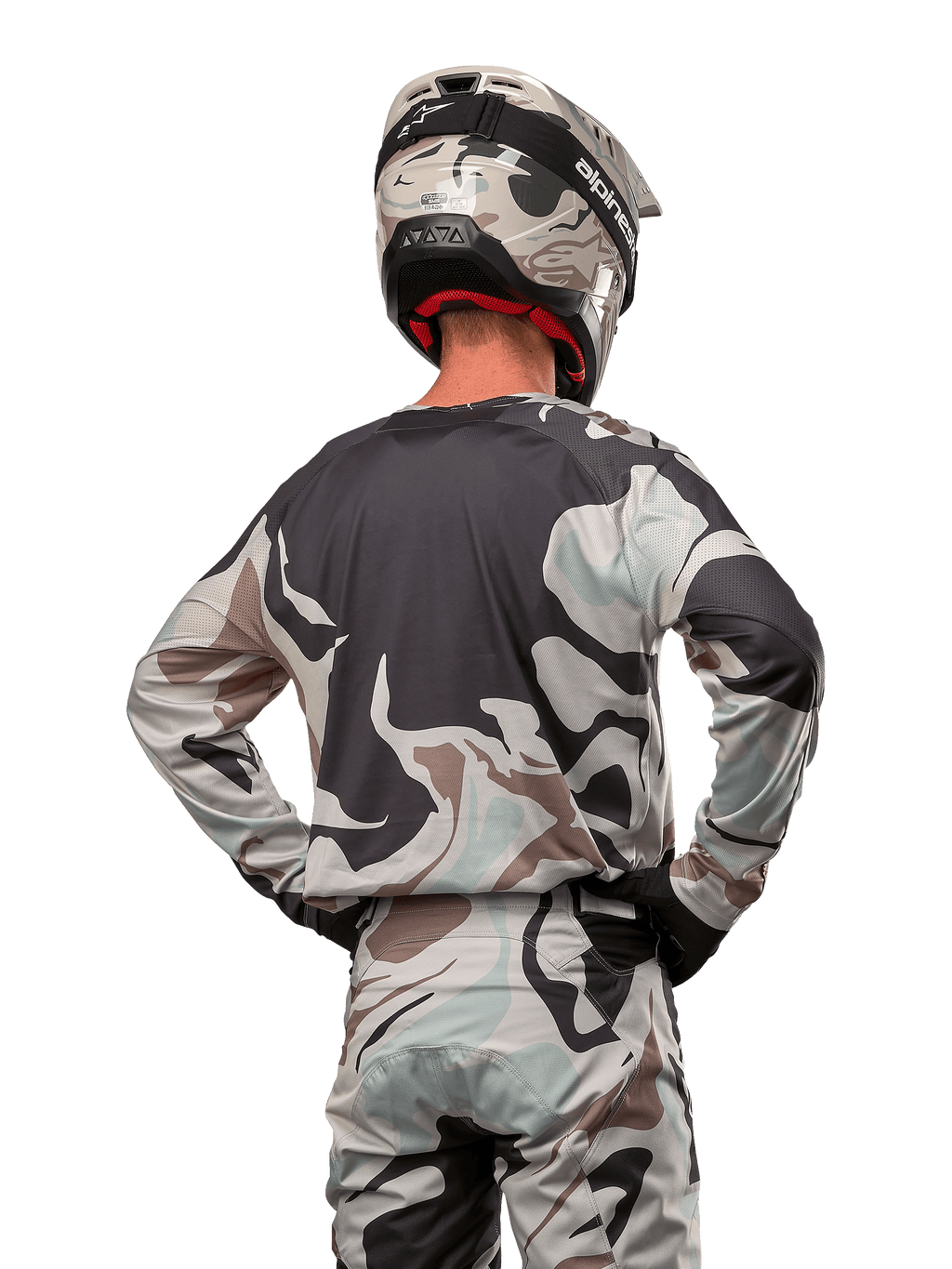Motocrossrijder van achteren gezien in de Alpinestars 2024 Racer Tactical Jersey in Iron Camo Dust Gray, bijpassende camouflagebroek en helm, handen op de heupen, gecoördineerde off-road race-uitrusting