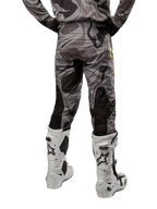 Alpinestars 2024 Racer Tactical broek, motorcrossbroek, Cast Gray Camo Magnet, achteraanzicht met camouflagepatroon en zwarte ademende stretchzones, gedragen met witte en zwarte motorcrosslaarzen, ontworpen voor off-road racen.