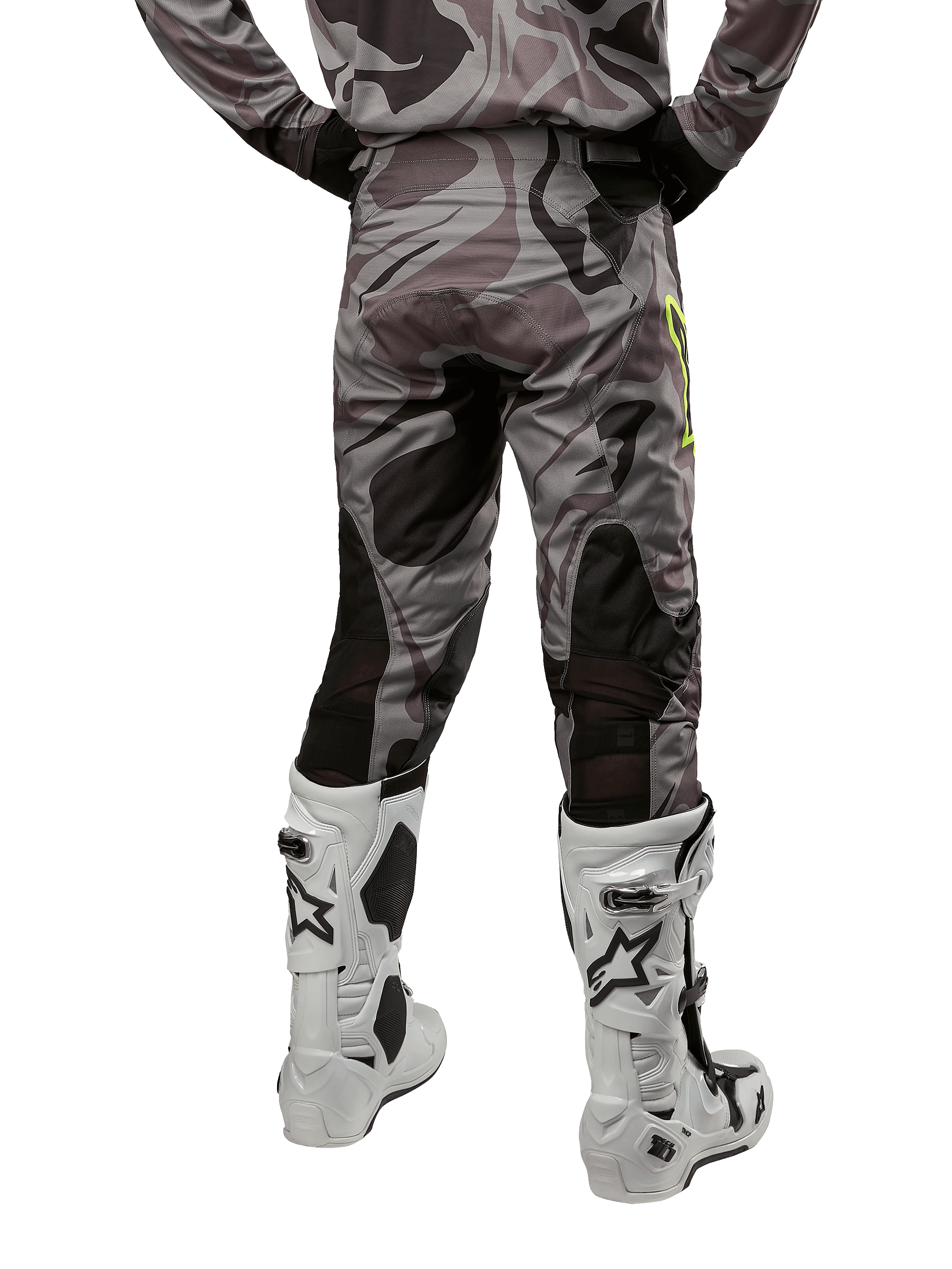 Alpinestars 2024 Racer Tactical broek, motorcrossbroek, Cast Gray Camo Magnet, achteraanzicht met camouflagepatroon en zwarte ademende stretchzones, gedragen met witte en zwarte motorcrosslaarzen, ontworpen voor off-road racen.