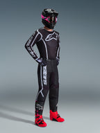 Alpinestars 2026 Fluid Apex Pants, Motocross Pants, Black and Gray, worn with matching black and white jersey, black helmet with pink goggles, and bright red boots, featuring bold white branding on the legs and a sport-fit design for off-road racing.
