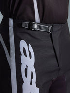 Alpinestars 2026 Fluid Apex Pants, Motocross Pants, Black and Gray, close-up detail of the integrated ratchet closure system for a secure fit, featuring white logo graphics on durable 600D polyfabric.