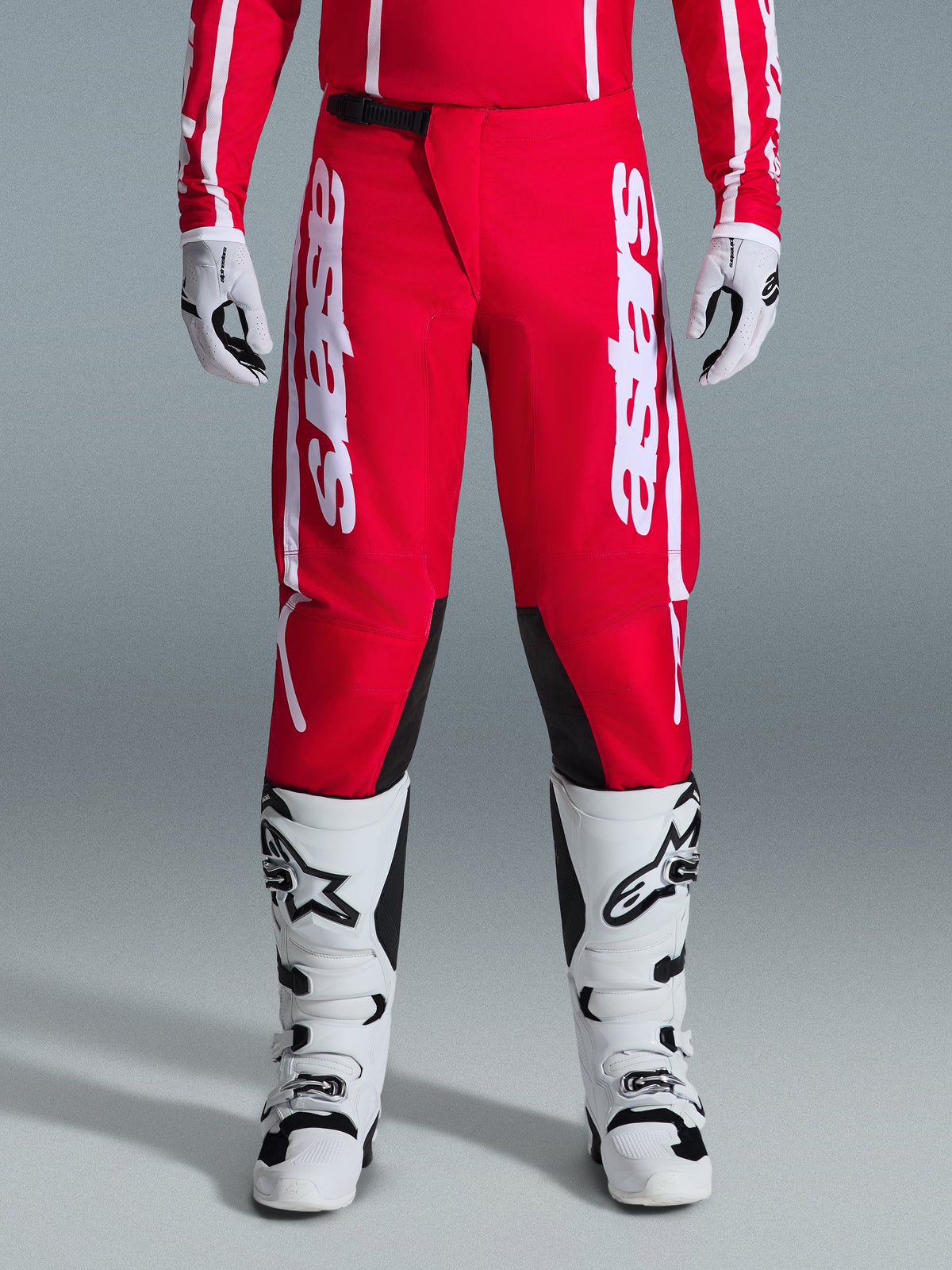 Alpinestars 2026 Fluid Apex broek, motorcrossbroek, rood met wit, voorzien van grote witte Astars-logo's op de dijen en zwarte panelen aan de binnenkant van de knieën, gedragen met bijpassende witte en zwarte laarzen en handschoenen voor een complete off-road racing look.