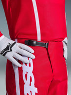 Alpinestars 2026 Fluid Apex Pants, Motocross Pants, Red and White, close-up of the black ratchet waist closure system, worn with white Alpinestars gloves and matching red jersey, durable performance gear for off-road riding.
