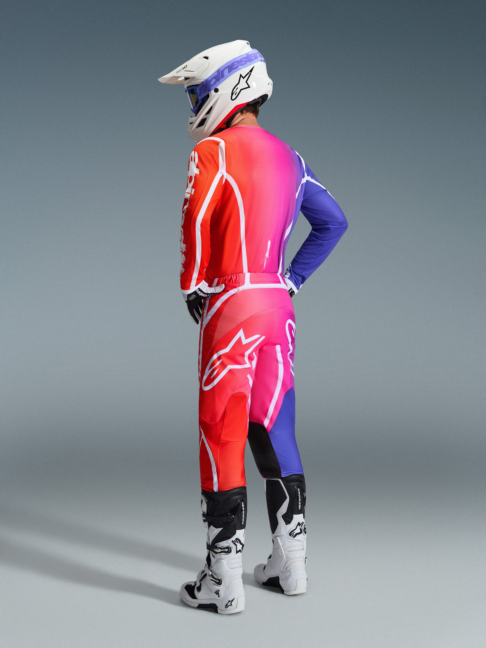 Alpinestars 2026 Fluid Apex-motorcrossuitrusting, multicolor jersey en broek met een rood, roze en paars kleurverloop, witte logo's, witte helm en witte laarzen, gecoördineerde outfit voor off-road racen