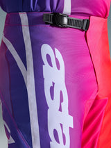 Alpinestars 2026 Fluid Apex Pants, motorcrossbroek, meerkleurig paars, roze en rood, close-up van de taille en heup met een zwarte ratelsluiting en groot wit verticaal Alpinestars-logo, levendig kleurverloop met duurzame polyfabric textuur