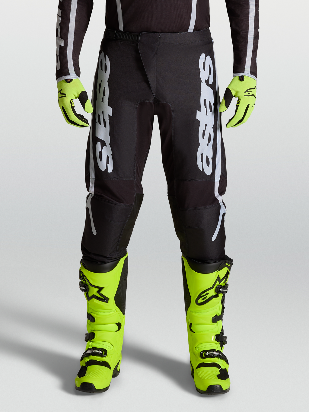 Alpinestars Fluid Apex V2 motocrossbroek voor heren, zwart en zilver, voorzien van ergonomische stretchpanelen en 600D-polystof, gedragen op een model.