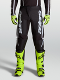 Alpinestars Fluid Apex V2 motocrossbroek voor heren, zwart en zilver, voorzien van ergonomische stretchpanelen en 600D-polystof, gedragen op een model.