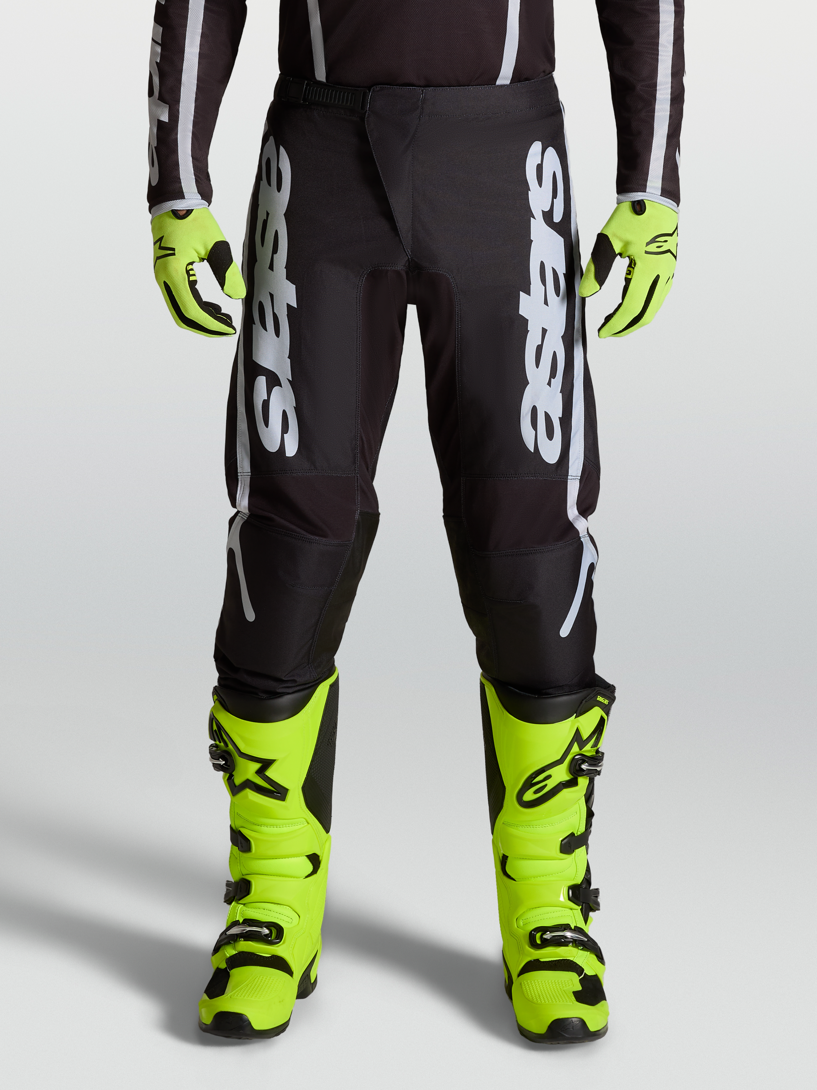 Alpinestars Fluid Apex V2 motocrossbroek voor heren, zwart en zilver, voorzien van ergonomische stretchpanelen en 600D-polystof, gedragen op een model.