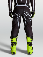 Alpinestars Fluid Apex V2 Broek, motocrossbroek in zwart en zilver, gedragen met fluorgele laarzen, ergonomische off-road pasvorm.