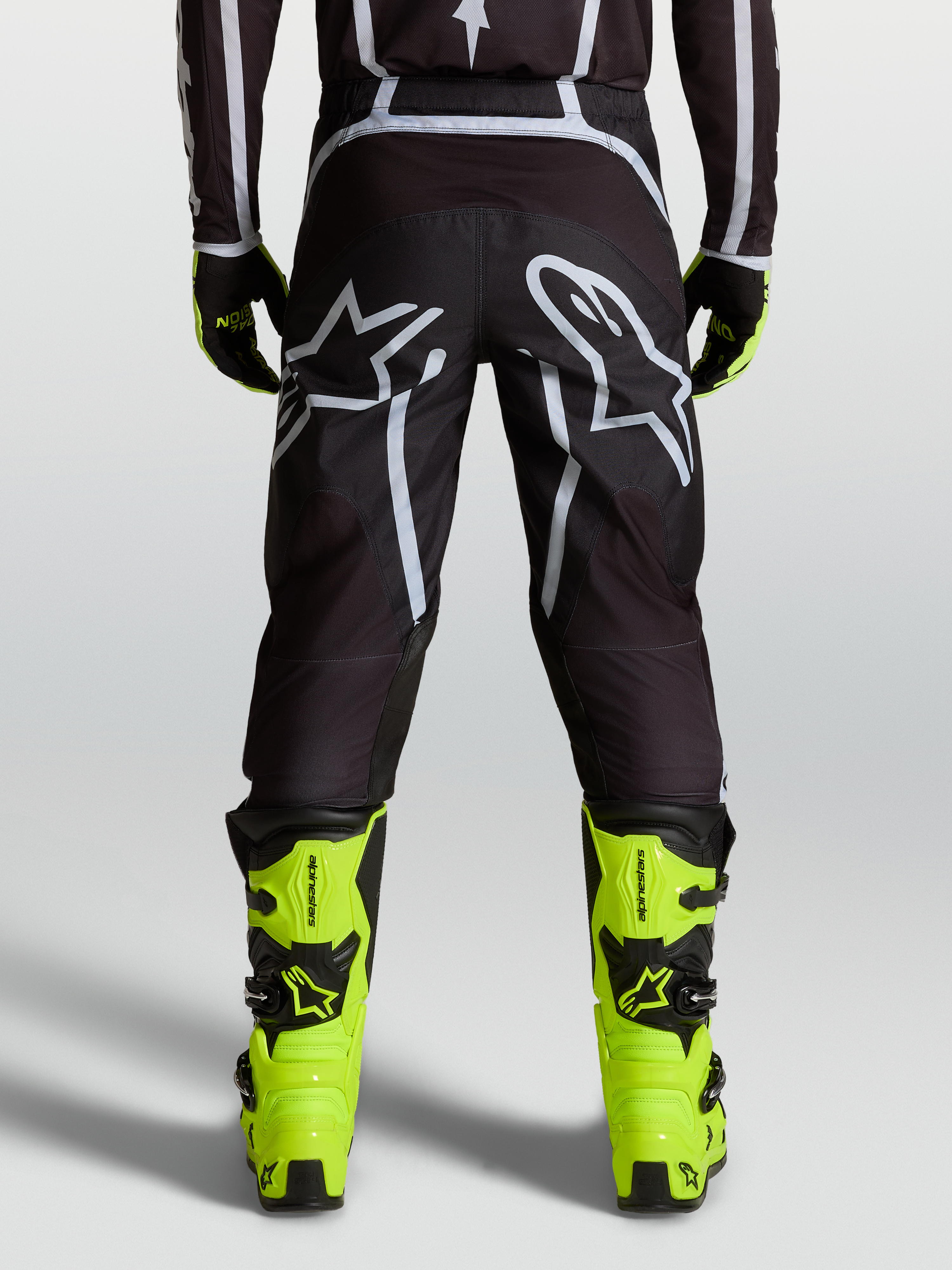 Alpinestars Fluid Apex V2 Broek, motocrossbroek in zwart en zilver, gedragen met fluorgele laarzen, ergonomische off-road pasvorm.