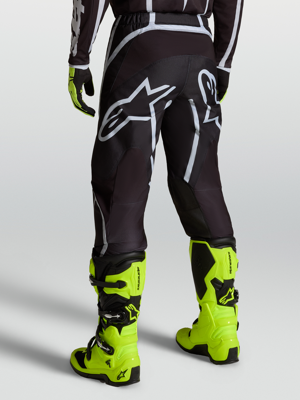 Alpinestars Fluid Apex V2 Broek, motocrossbroek voor heren, zwart en zilver, gedragen met gele motorlaarzen.