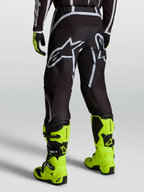 Alpinestars Fluid Apex V2 Broek, motocrossbroek voor heren, zwart en zilver, gedragen met gele motorlaarzen.