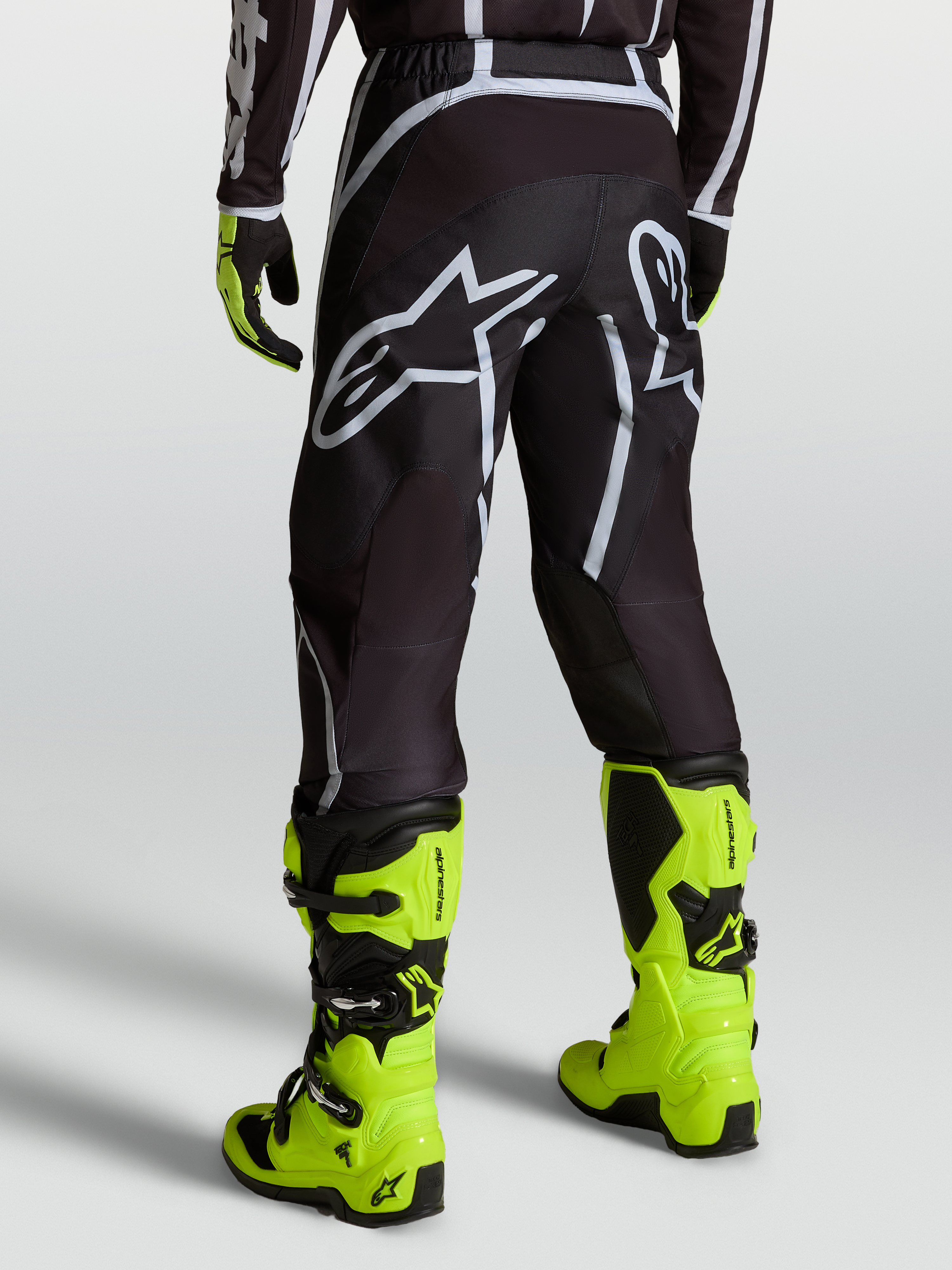 Alpinestars Fluid Apex V2 Broek, motocrossbroek voor heren, zwart en zilver, gedragen met gele motorlaarzen.