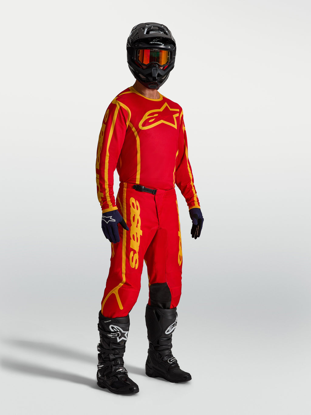 Alpinestars Fluid Apex V2 broek, herenmotocrossbroek in rood en goud, gedragen met jersey en laarzen voor off-road.