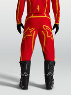 Alpinestars Fluid Apex V2 broek, heren-motocrossbroek in rood en goud, achteraanzicht met zwarte motorlaarzen.