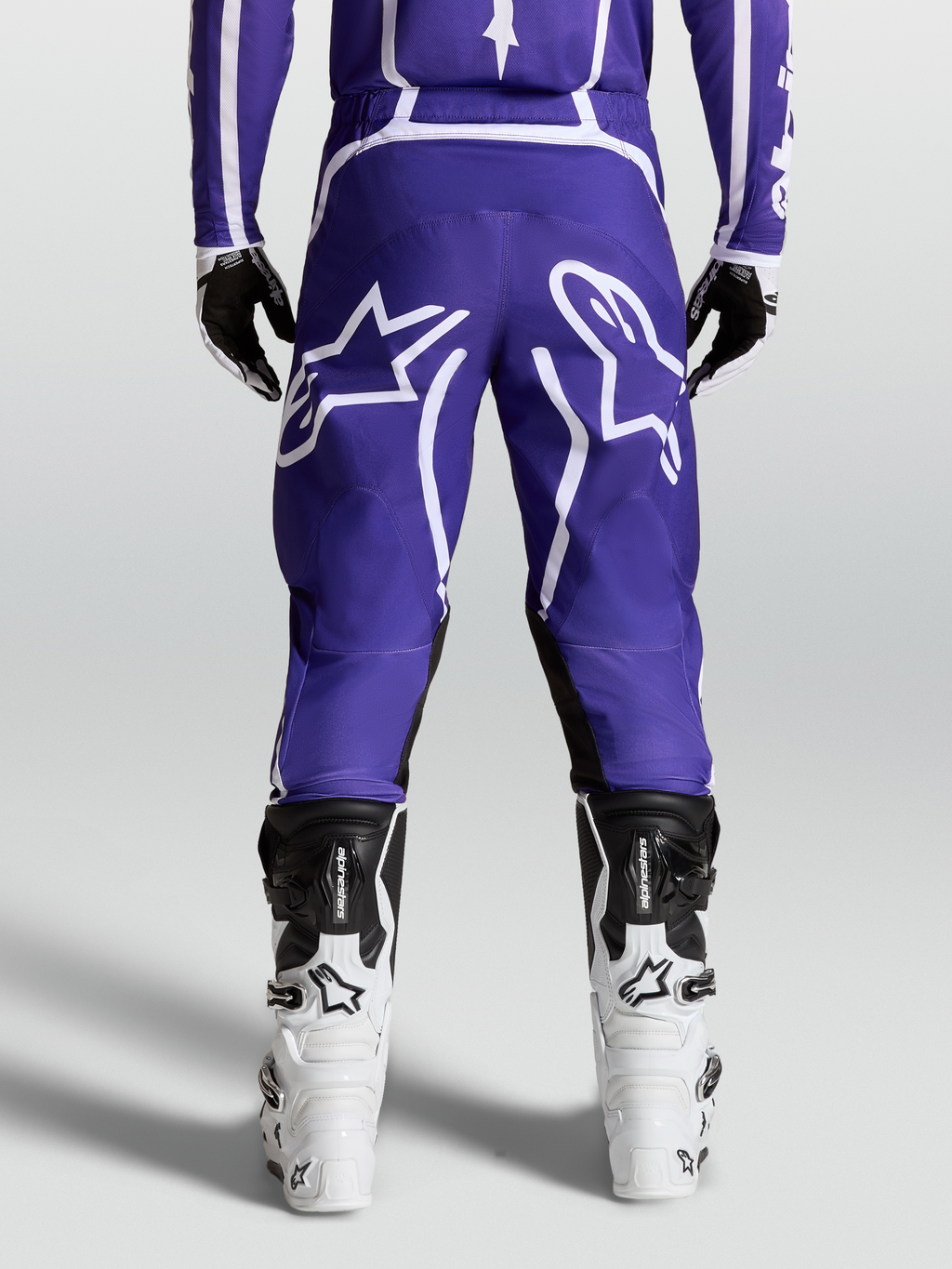 Alpinestars Fluid Apex V2 broek, motocross- en off-roadbroek voor heren, blauw en wit, achteraanzicht op model met motorlaarzen en 600D polyfabric constructie.