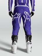 Alpinestars Fluid Apex V2 broek, motocross- en off-roadbroek voor heren, blauw en wit, achteraanzicht op model met motorlaarzen en 600D polyfabric constructie.