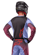 Motorcrossrijder van achteren in Alpinestars 2024 Racer Hoen uitrusting, Lavan Purple en zwart jersey met rood logo, bijpassende broek met rode accenten, zwarte helm, gecoördineerde outfit voor off-road racen