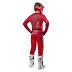 Alpinestars 2024 Racer Hoen broek en bijpassende jersey in Mars Red Burgundy, achteraanzicht van een motorcrossrijder in volledige uitrusting inclusief een rode helm en witte laarzen, toont de sportieve pasvorm en branding voor off-road racen.
