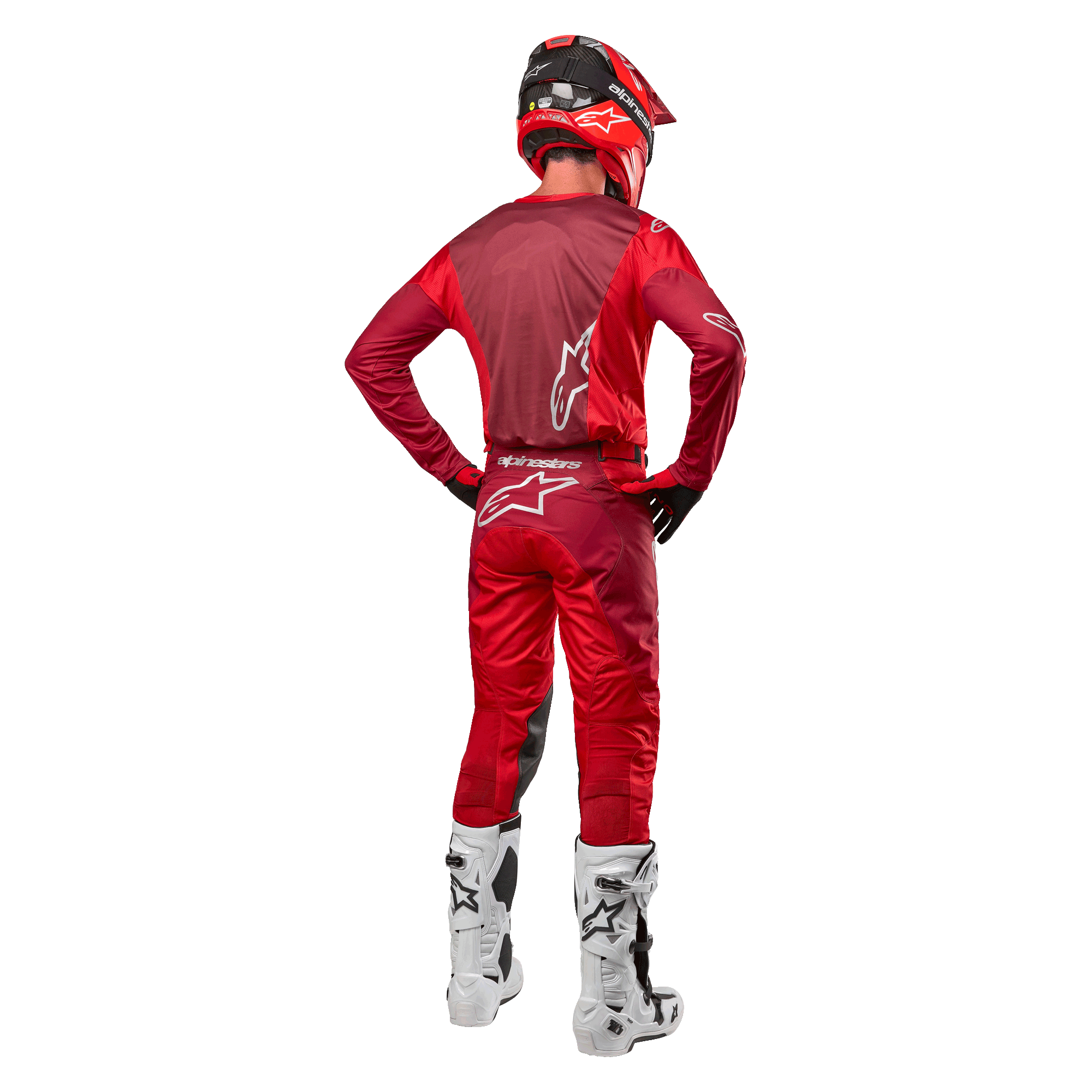 Alpinestars 2024 Racer Hoen broek en bijpassende jersey in Mars Red Burgundy, achteraanzicht van een motorcrossrijder in volledige uitrusting inclusief een rode helm en witte laarzen, toont de sportieve pasvorm en branding voor off-road racen.