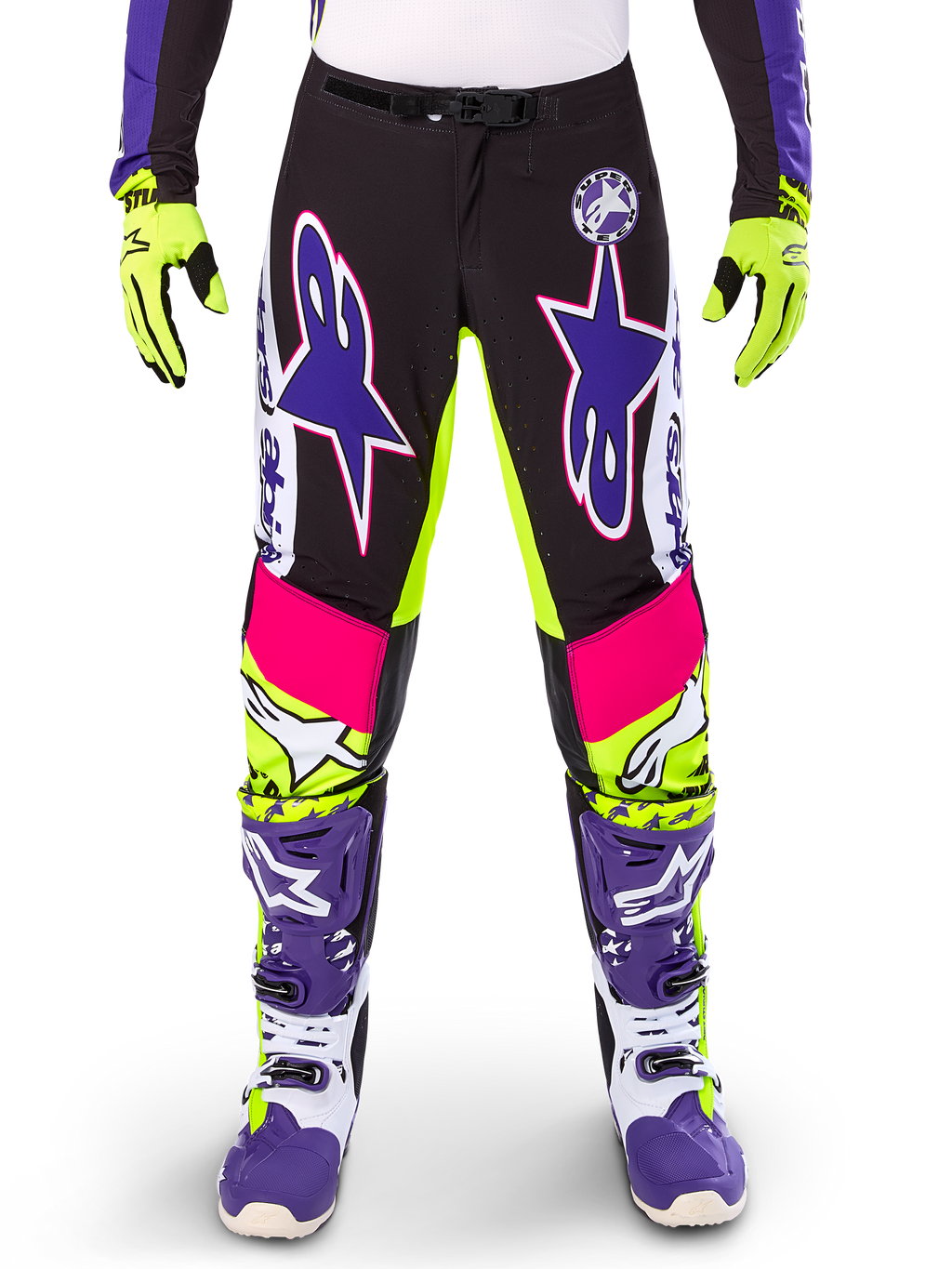 Alpinestars Limited Edition Supertech Dirt Studios motorbroek, motorcrossbroek, wit, paars en neongeel, voorzien van zwarte panelen met neongele en roze accenten, grote paarse sterlogo's, getoond met bijpassende neongele handschoenen en paarse racelaarzen, duurzame off-road racekleding