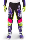 Alpinestars Limited Edition Supertech Dirt Studios motorbroek, motorcrossbroek, wit, paars en neongeel, voorzien van zwarte panelen met neongele en roze accenten, grote paarse sterlogo's, getoond met bijpassende neongele handschoenen en paarse racelaarzen, duurzame off-road racekleding