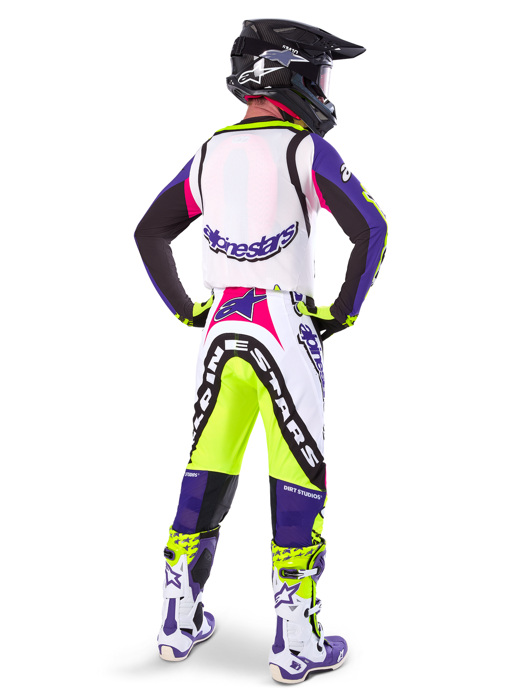 Alpinestars Limited Edition Supertech Dirt Studios® crossbroek in White Purple en Yellow Fluo, motocrossrijder vanaf de achterkant gezien met bijpassende jersey, laarzen en zwarte carbon helm, professionele off-road race-uitrusting met opvallende graphics en neonaccenten.