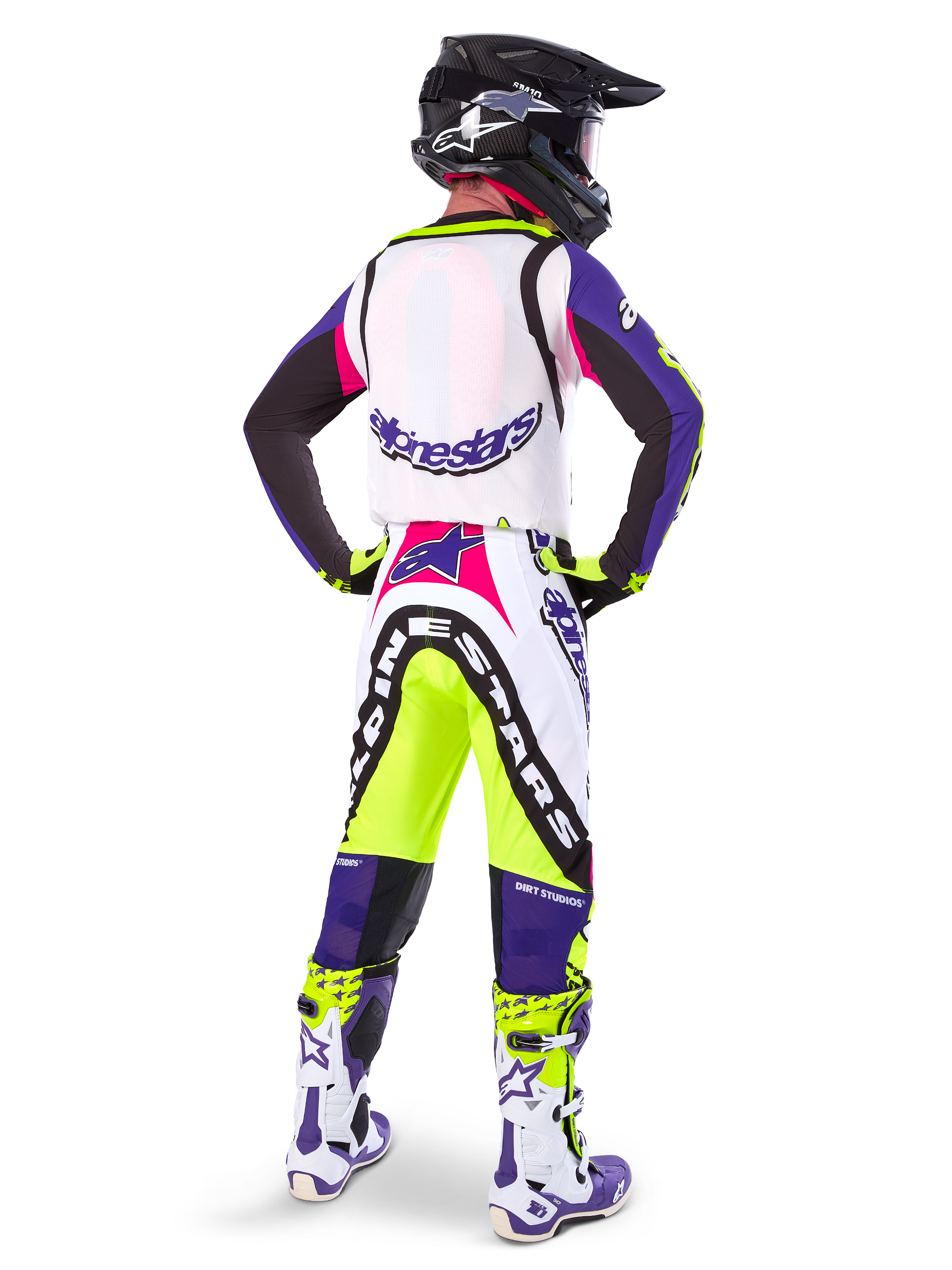 Alpinestars Limited Edition Supertech Dirt Studios® crossbroek in White Purple en Yellow Fluo, motocrossrijder vanaf de achterkant gezien met bijpassende jersey, laarzen en zwarte carbon helm, professionele off-road race-uitrusting met opvallende graphics en neonaccenten.