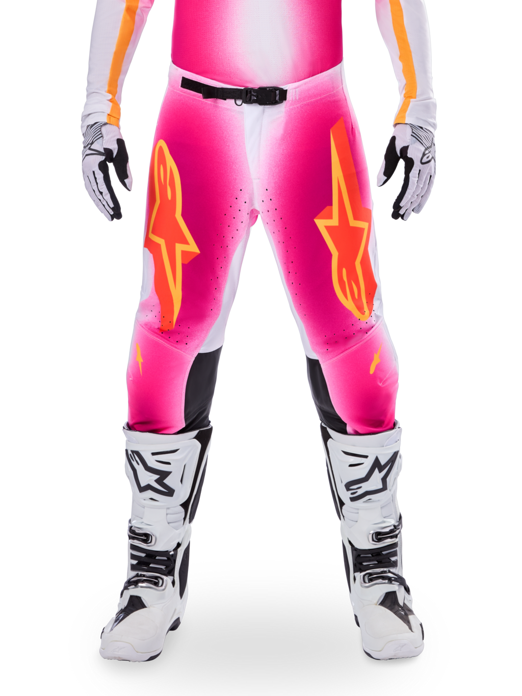 Alpinestars Limited Edition Supertech AFD MIG Pants, motorcrossbroek, fluo roze en wit met oranje accenten, met grote sterlogo's op de bovenbenen, geperforeerde panelen en zwarte knie-gripzones, gedragen met witte en zwarte motorcrosslaarzen