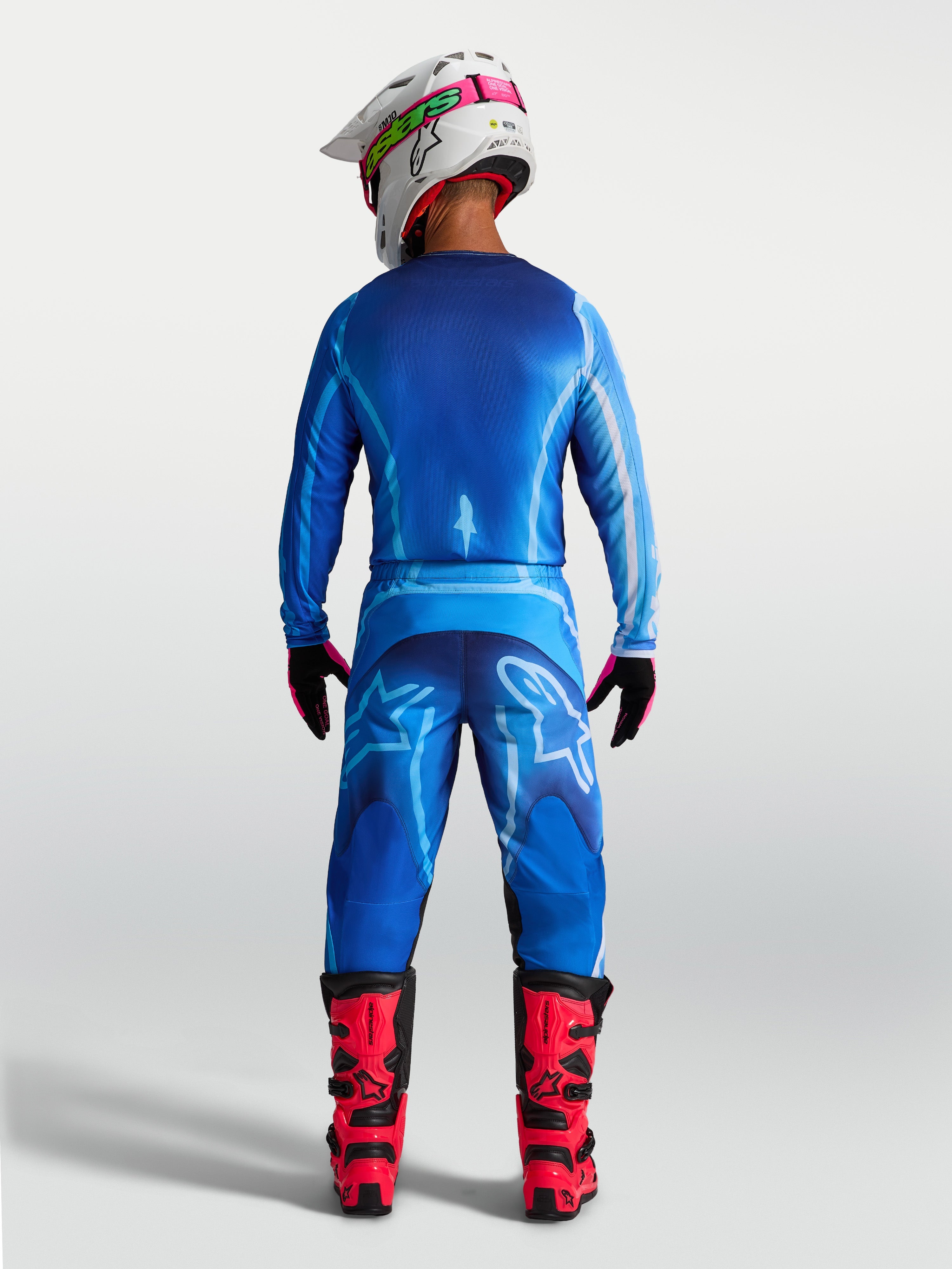 Alpinestars Fluid Kepler Broek, heren motorcrossbroek in UCLA blauw, achteraanzicht met ergonomische pasvorm en duurzame polystof, gedragen met rode laarzen voor off-road racing.