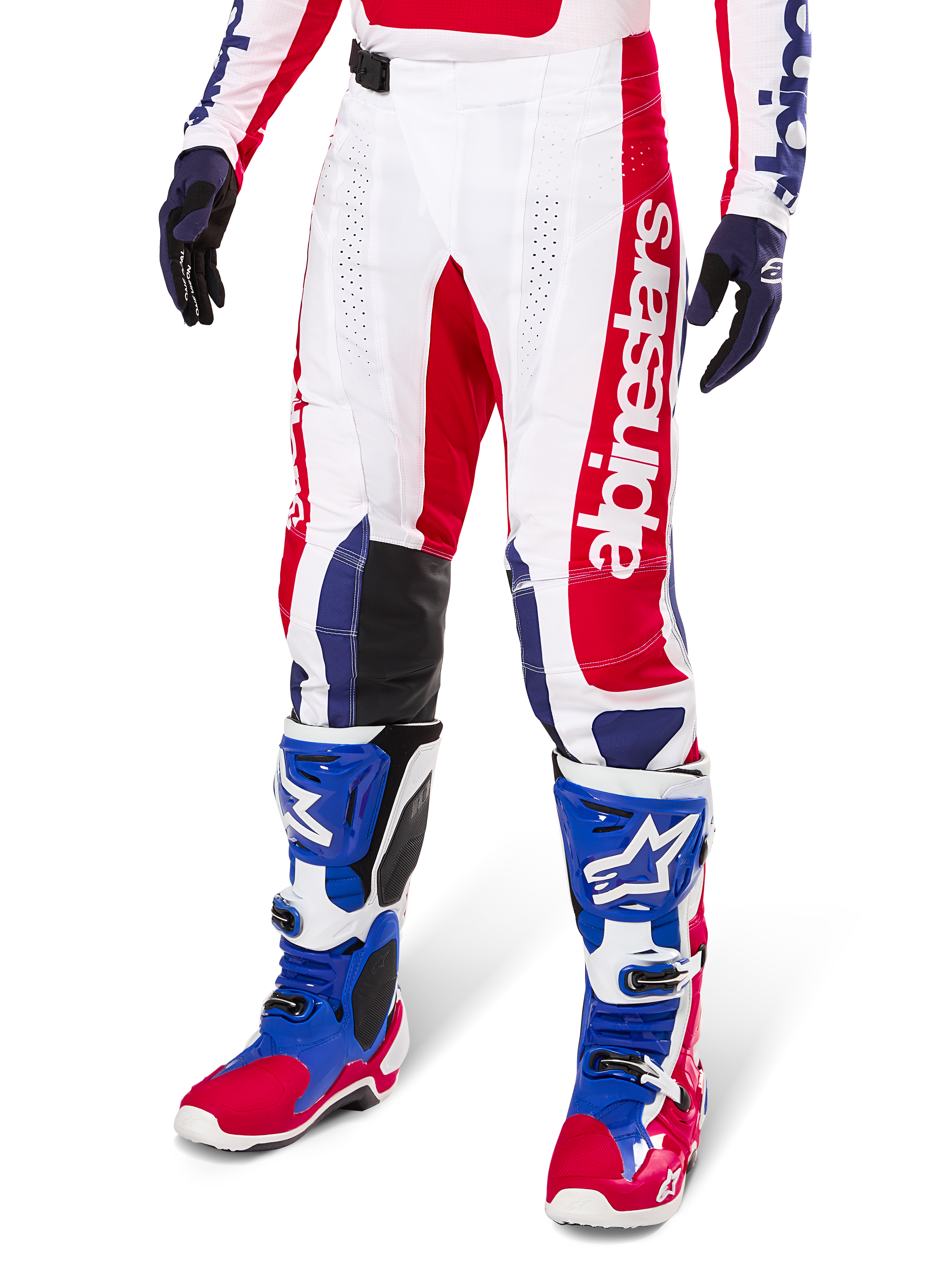 Alpinestars Limited Edition Techstar Fortitude crossbroek, motorcross broek, helder rood, wit en blauw, gedragen met bijpassende off-road laarzen en handschoenen, voorzien van verticale branding op de broekspijp, ademende geperforeerde panelen en zwarte verstevigde kniestukken, atletisch race-ontwerp