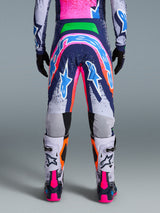 Motorcrosser van achteren gezien, draagt Alpinestars Limited Edition Supertech Records broek, meerkleurig ontwerp met felroze, marineblauwe en oranje accenten, bijpassende jersey en wit-roze laarzen, voorzien van opvallende branding en ster-graphics