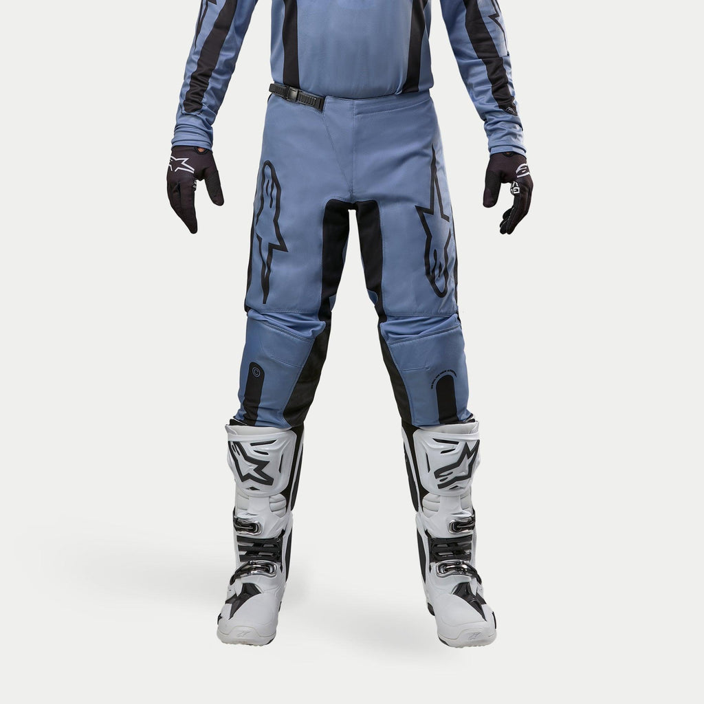 Alpinestars 2024 Fluid Lurv crossbroek, motorcross broek, lichtblauw en zwart, gedragen met witte en zwarte racelaarzen en bijpassende handschoenen, voorzien van opvallende zwarte sterlogo's op de dijen, ergonomisch ontwerp voor off-road prestaties
