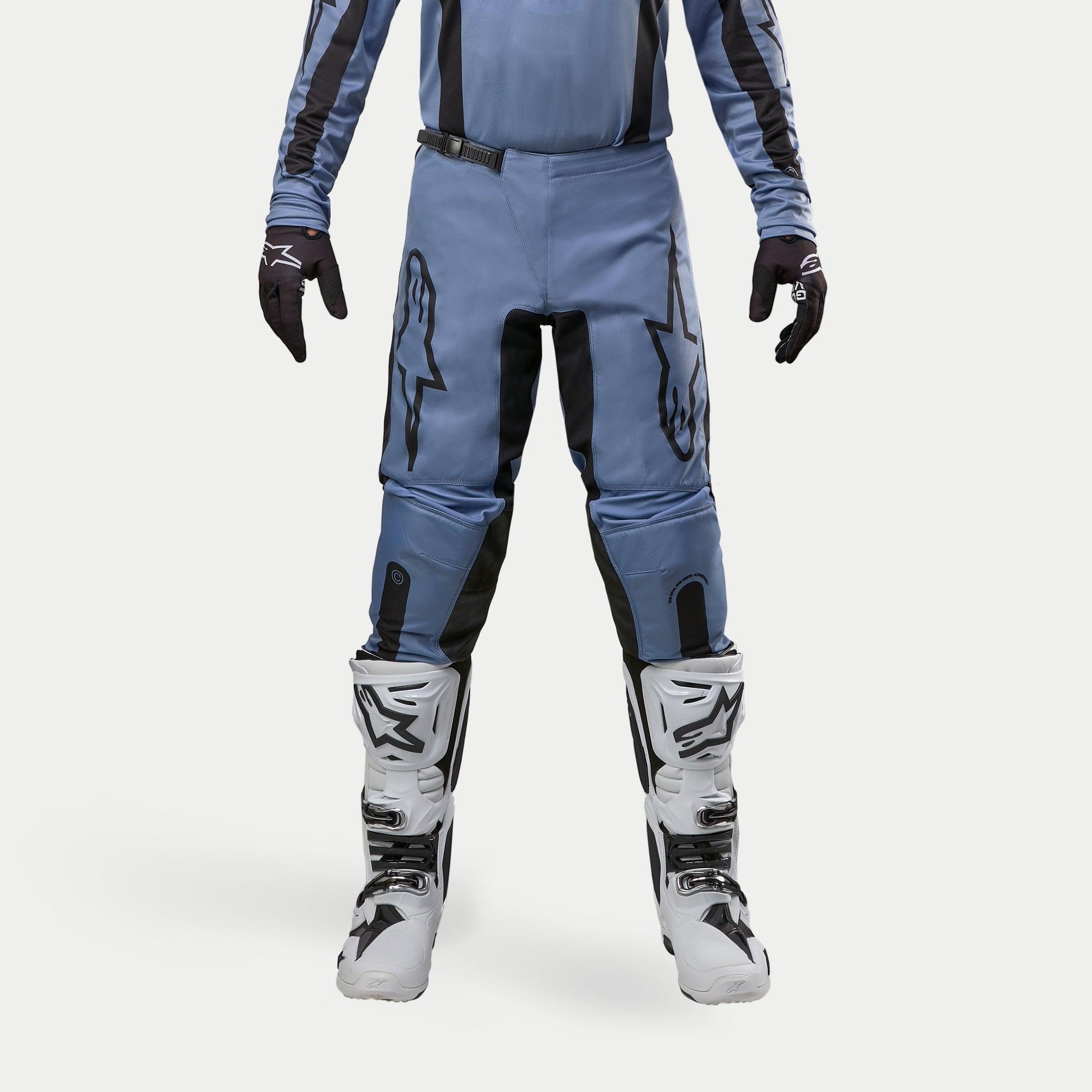 Alpinestars 2024 Fluid Lurv crossbroek, motorcross broek, lichtblauw en zwart, gedragen met witte en zwarte racelaarzen en bijpassende handschoenen, voorzien van opvallende zwarte sterlogo's op de dijen, ergonomisch ontwerp voor off-road prestaties