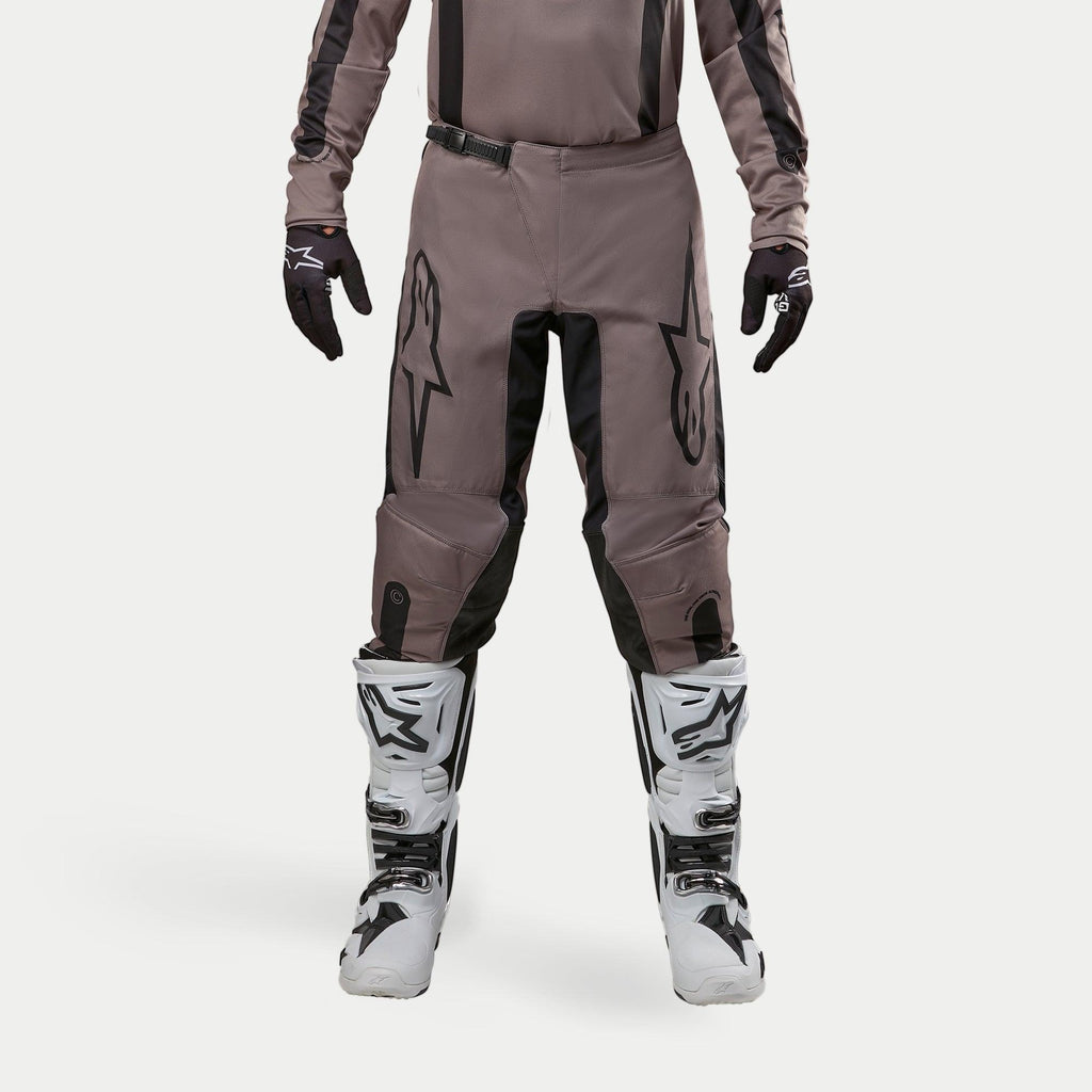 Alpinestars 2024 Fluid Lurv broek, motorcross broek, Mud Black, gedragen met bijpassend jersey, zwarte handschoenen en witte laarzen, voorzien van grote zwarte logo's op de dijbenen, ergonomische pasvorm en duurzaam materiaal voor off-road racen