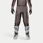 Alpinestars 2024 Fluid Lurv broek, motorcross broek, Mud Black, gedragen met bijpassend jersey, zwarte handschoenen en witte laarzen, voorzien van grote zwarte logo's op de dijbenen, ergonomische pasvorm en duurzaam materiaal voor off-road racen