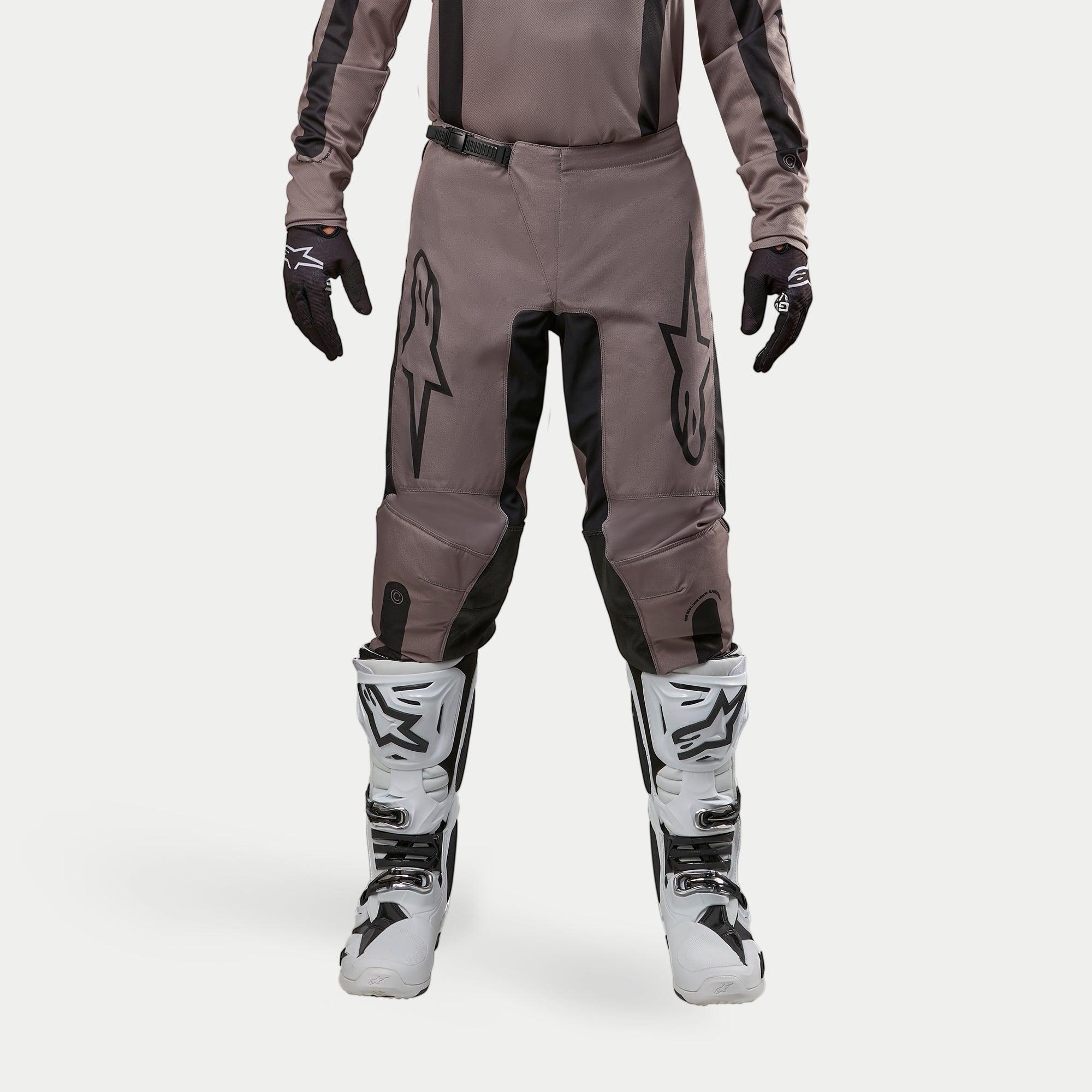 Alpinestars 2024 Fluid Lurv broek, motorcross broek, Mud Black, gedragen met bijpassend jersey, zwarte handschoenen en witte laarzen, voorzien van grote zwarte logo's op de dijbenen, ergonomische pasvorm en duurzaam materiaal voor off-road racen